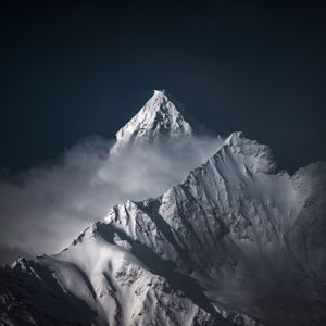 Fotobehang van een scherpe, besneeuwde bergtop die boven de wolken uitsteekt tegen een donkere achtergrond